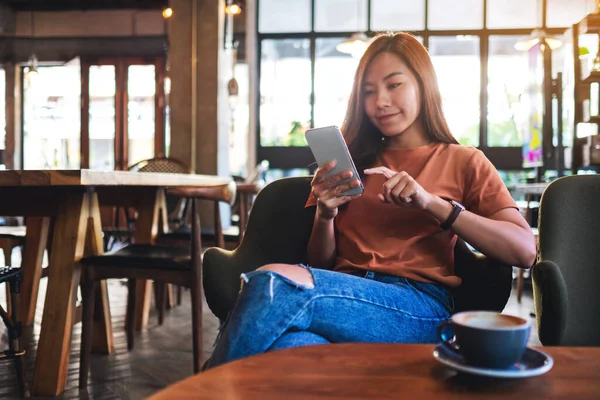 Kafede cep telefonu tutan ve kullanan Asyalı güzel bir kadının yakın plan görüntüsü.