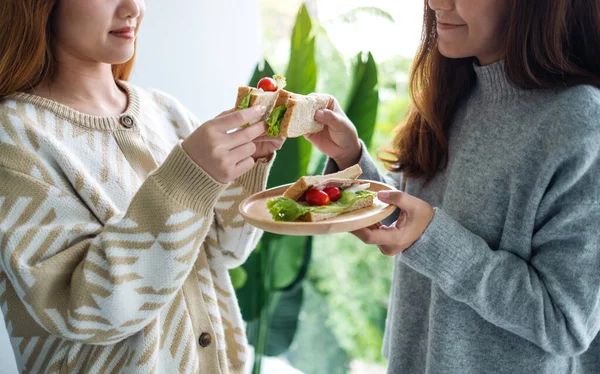 İki kadın, tahtadan tabakta kepekli sandviçi birlikte tutuyor ve yiyorlar.