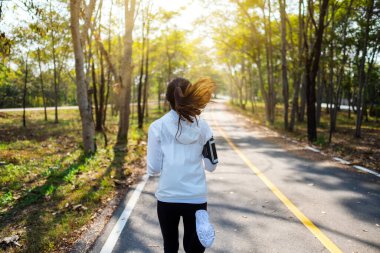 Sabahları şehir parkında koşan Asyalı bir kadının arka plan görüntüsü.