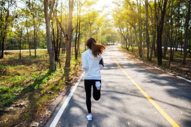 Sabahları şehir parkında koşan Asyalı bir kadının arka plan görüntüsü.
