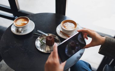 Kafede yemek yemeden önce kahve ve atıştırmalık fotoğraf çeken bir kadın.