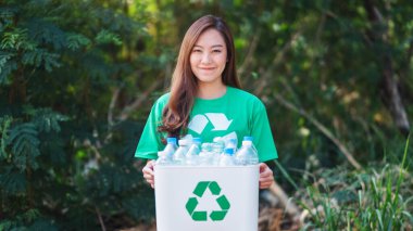 An asian woman collecting garbage and holding a recycle bin with plastic bottles in the outdoors