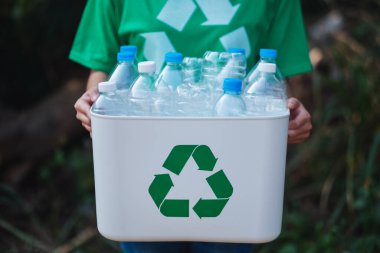 Çöp toplayan ve elinde plastik şişelerle geri dönüşüm kutusunu tutan bir kadın.