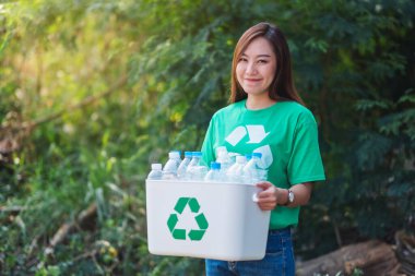 An asian woman collecting garbage and holding a recycle bin with plastic bottles in the outdoors