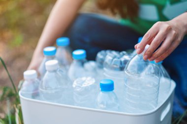 A woman collecting garbage plastic bottles into a recycle bin in the outdoors