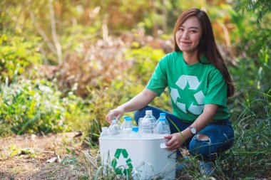 An asian woman collecting garbage plastic bottles into a recycle bin in the outdoors