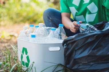 A woman picking up garbage plastic bottles into a box and bag for recycling concept