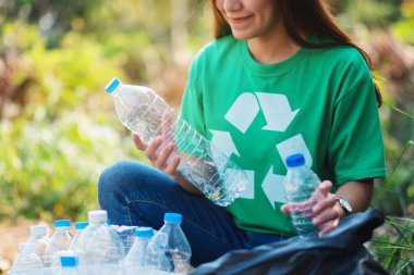 A woman picking up garbage plastic bottles into a box and bag for recycling concept