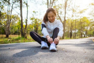 Yakından bakınca bir kadın koşucunun ayakkabı bağcıklarını bağlayıp şehir parkında koşuya hazırlandığını görüyoruz.