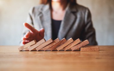 Bir iş adamının yakın plan görüntüsü, iş çözümü kavramı için tahta domino taşlarını engellemeye çalışıyor. 