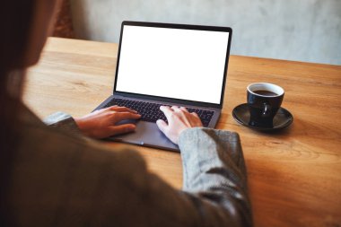 Kafedeki boş beyaz masaüstü ekran ile dizüstü bilgisayarı kullanan ve yazan bir kadının görüntüsü