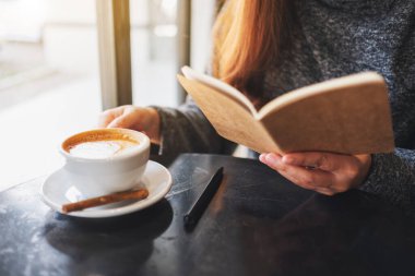 Closeup image of a woman reading a book while drinking coffee in cafe 