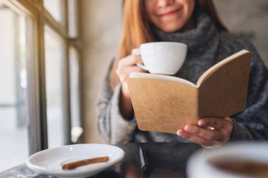 Kafede kahve içerken kitap okuyan Asyalı güzel bir kadının yakın plan görüntüsü. 