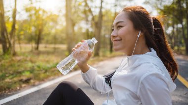 Şehir parkında koştuktan sonra şişeden su içen Asyalı bir koşucunun yakın plan görüntüsü.