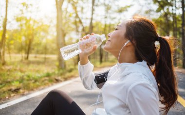 Şehir parkında koştuktan sonra şişeden su içen Asyalı bir koşucunun yakın plan görüntüsü.