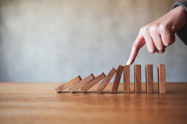 Bir parmağın yakın plan görüntüsü, iş çözümü kavramı için tahta domino taşlarını durdurmaya çalış. 
