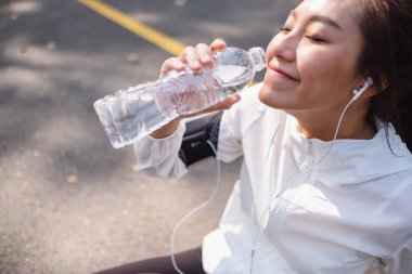 Şehir parkında koştuktan sonra şişeden su içen Asyalı bir koşucunun yakın plan görüntüsü.