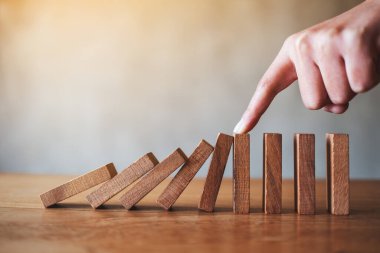 Bir parmağın yakın plan görüntüsü, iş çözümü kavramı için tahta domino taşlarını durdurmaya çalış. 