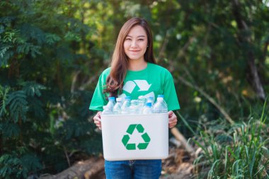 A beautiful asian woman collecting garbage and holding a recycle bin with plastic bottles in the outdoors