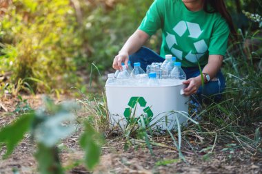 A woman collecting garbage plastic bottles into a recycle bin in the outdoors