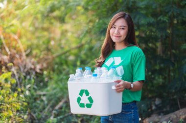 A beautiful asian woman collecting garbage and holding a recycle bin with plastic bottles in the outdoors