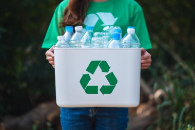 Çöp toplayan ve elinde plastik şişelerle geri dönüşüm kutusunu tutan bir kadın.