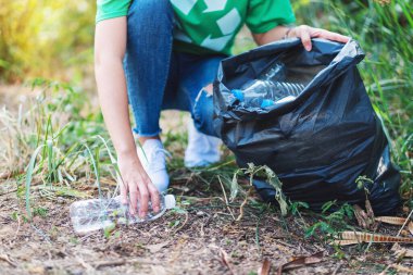 Geri dönüşüm konsepti için plastik şişeleri poşete dolduran bir kadının yakın plan görüntüsü.