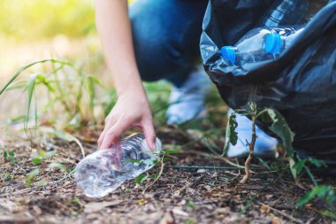 Closeup image of a woman picking up garbage plastic bottles into a bag for recycling concept