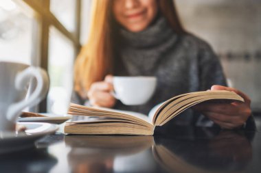 Closeup image of a beautiful woman reading a book while drinking coffee in the morning