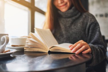 Closeup image of a beautiful woman holding and reading a book with coffee cup on the table