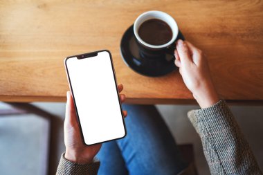 Kafede otururken elinde boş masaüstü ekranıyla siyah cep telefonu tutan bir kadının üst görünüm görüntüsü