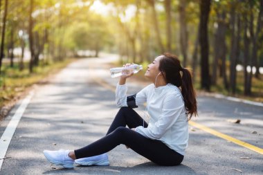 Şehir parkında koştuktan sonra şişeden su içen Asyalı bir koşucunun yakın plan görüntüsü.