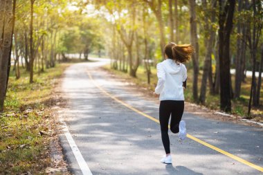 Sabahları şehir parkında koşan Asyalı bir kadının arka plan görüntüsü.