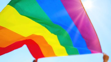 People holding and raising a rainbow flag over the blue sky