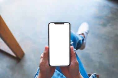 Kafede otururken elinde beyaz ekranlı siyah cep telefonu olan bir kadının üst görünüm görüntüsü