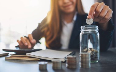 Bir iş kadınının cam kavanoza para istiflediği ve koyduğu yakın plan görüntüsü. 