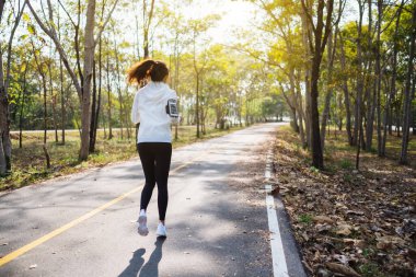 Sabahları şehir parkında koşan Asyalı bir kadının arka plan görüntüsü.