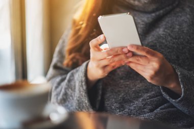 Kafe 'de elinde kahve fincanı olan ve cep telefonu kullanan bir kadının yakın plan fotoğrafı.