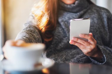 Kafede kahve içerken cep telefonu tutan ve kullanan bir kadının yakın plan fotoğrafı.