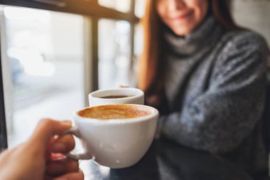 Closeup image of a woman and a man clinking coffee mugs in cafe