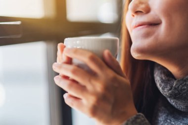 Asyalı güzel bir kadının bir fincan sıcak kahveyi kucağında tutarken ve koklarken görüntüsü.