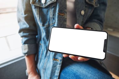 Kafede elinde siyah cep telefonu tutan ve gösteren bir kadının görüntüsü.