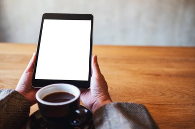 Siyah tabletli, beyaz ekranlı ve ahşap masada kahve fincanı olan bir kadının görüntüsü. 