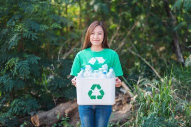 A beautiful asian woman collecting garbage and holding a recycle bin with plastic bottles in the outdoors