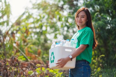 A beautiful asian woman collecting garbage and holding a recycle bin with plastic bottles in the outdoors