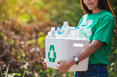 A beautiful asian woman collecting garbage and holding a recycle bin with plastic bottles in the outdoors