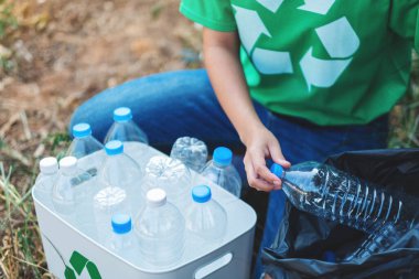Geri dönüşüm konsepti için plastik poşet ve kutuya çöp şişesi koyan bir kadın.