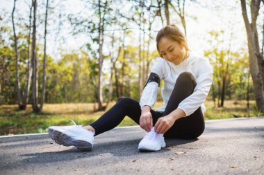 Yakından bakınca bir kadın koşucunun ayakkabı bağcıklarını bağlayıp şehir parkında koşuya hazırlandığını görüyoruz.