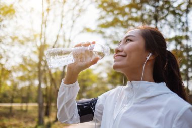 Şehir parkında koştuktan sonra şişeden su içen Asyalı bir koşucunun yakın plan görüntüsü.