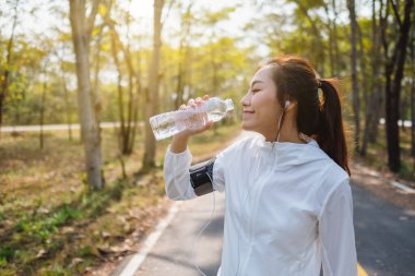 Şehir parkında koştuktan sonra şişeden su içen Asyalı bir koşucunun yakın plan görüntüsü.